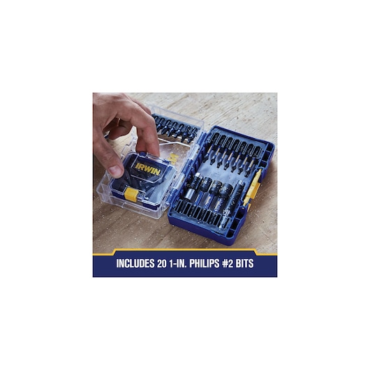 A hand opening a blue IRWIN branded plastic case containing multiple screwdriver bits, arranged in rows. The case includes 20 one-inch Philips #2 bits, with additional bits and accessories organized inside.