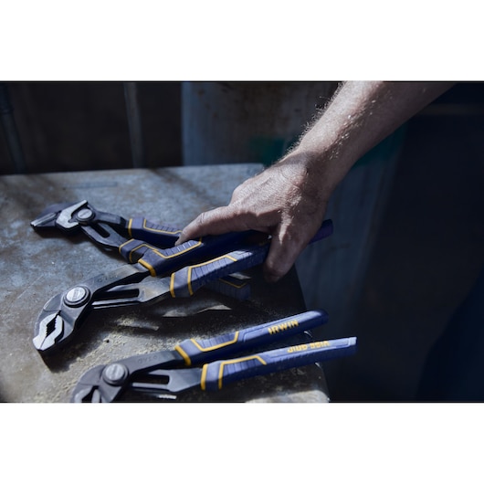 Photo of IRWIN 2078112 groove joint pliers with blue and yellow handles being picked up from a workbench.