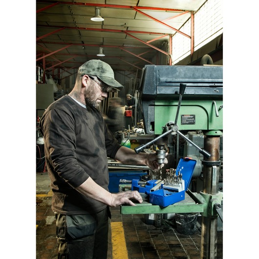 Photo of worker using IRWIN 10503730 drill bit set near a large drill press in a workshop setting.