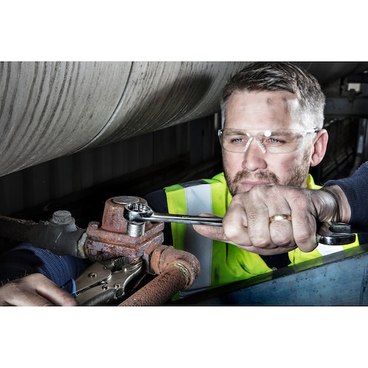 IRWIN 10504634 ratcheting wrench tightening a rusty pipe fitting, person in high-visibility vest using the tool.