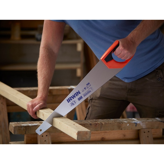 Photo of IRWIN 10505213 hand saw with orange handle cutting a wooden plank in a workshop.