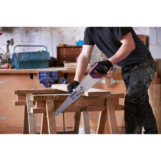 IRWIN 10505215 hand saw with purple handle cutting wood in workshop, gloved hand holding saw.