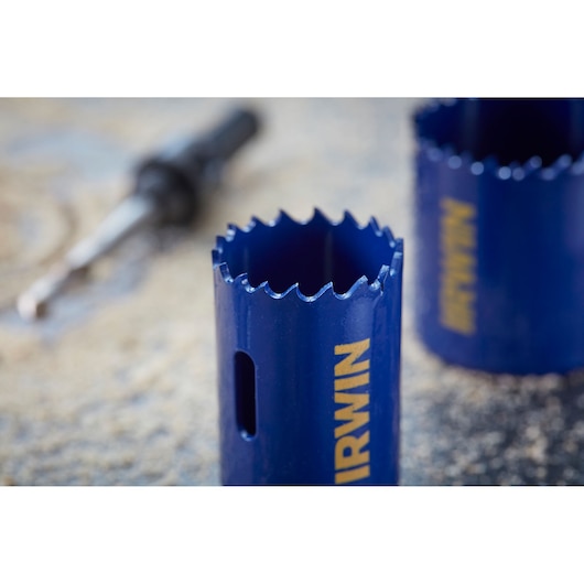 Close-up of IRWIN 10506445 blue hole saw with sharp teeth, drill bit blurred in background.