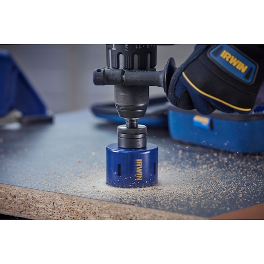 IRWIN 10506445 hole saw attached to drill cutting through wood, worker wearing IRWIN branded gloves.