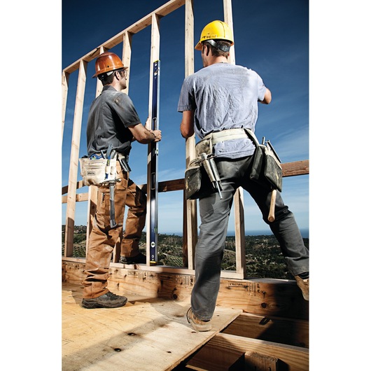 Photo of two construction workers using an IRWIN 1794067 level tool to check wall alignment, wearing tool belts and helmets.