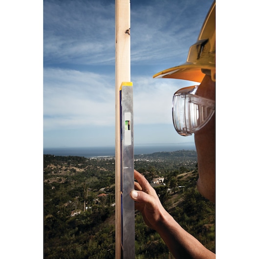 Photo of IRWIN 1794069 level tool held vertically against wood post outdoors, person wearing hard hat and safety glasses.