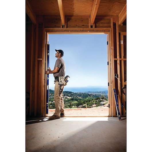 IRWIN 1794069 box beam level on floor next to door frame, construction worker installing door with scenic view.