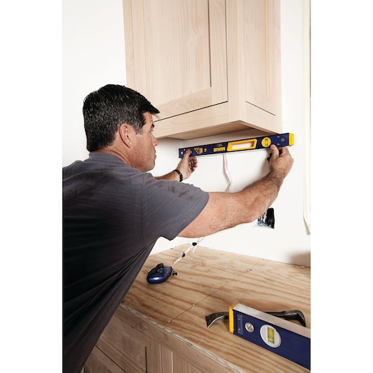 Photo of person using IRWIN level 1794075 to align wooden cabinets on a wall during installation.