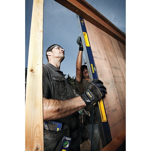 Photo of worker using IRWIN 1794077 spirit level on wooden frame, wearing IRWIN gloves, outdoor construction site.