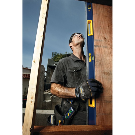 IRWIN 1794077 blue and yellow box beam level held vertically by a worker with gloves at a construction site.