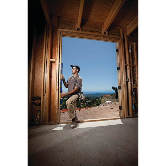 IRWIN 1794077 box beam level held vertically by worker inside wooden house frame with outdoor view.