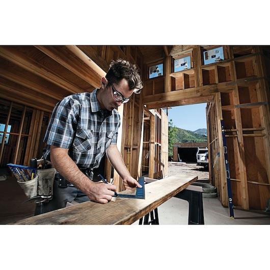 Photography of a person using an IRWIN tool to measure wood inside a building under construction, SKU 1794447.