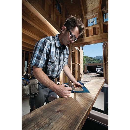 Worker using IRWIN 1794447 blue rafter square to mark wood beam at construction site.