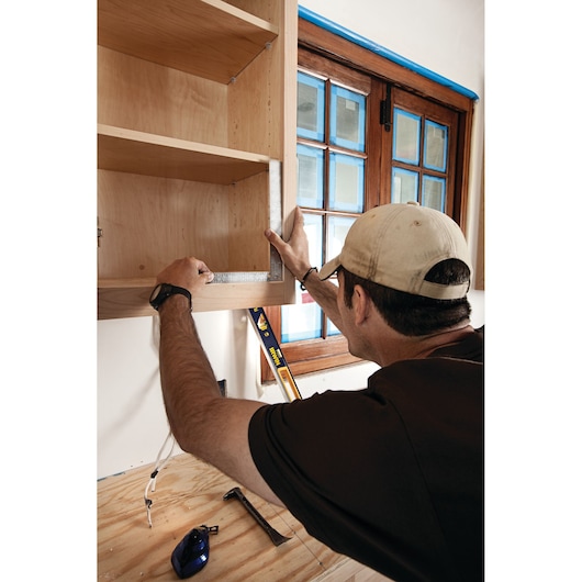 IRWIN 1794462 square tool used to measure inside a wooden cabinet near a window during installation.