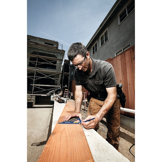 IRWIN 1794463 carpenter using blue speed square to mark a wooden beam at a construction site.