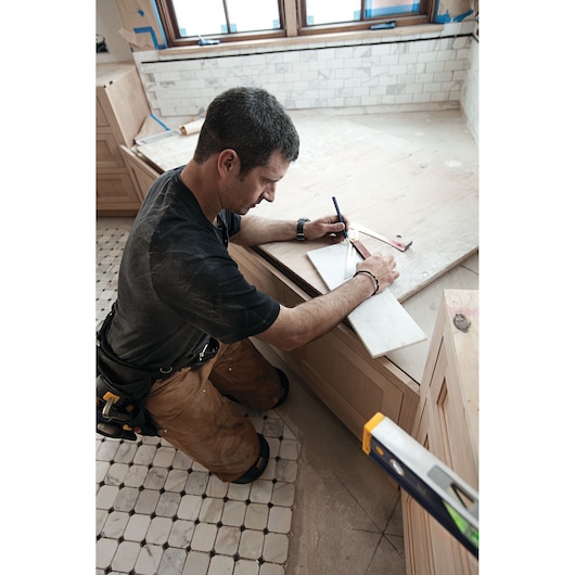 IRWIN 1794474 carpenter kneeling, using a square to mark measurements on tile during kitchen renovation.