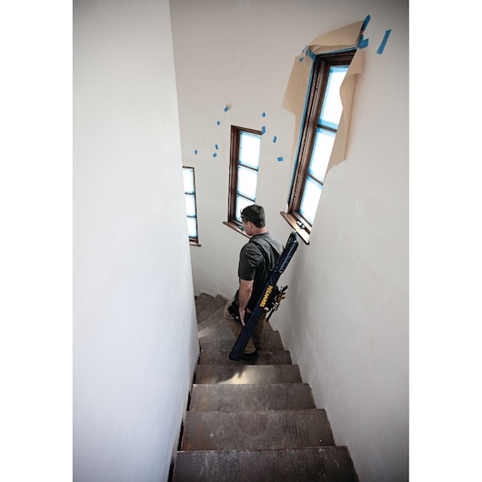 IRWIN 1804138 carrying case with strap carried by person walking down unfinished stairs, windows taped for painting.