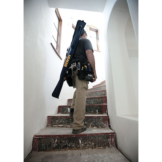 Photo of a worker carrying an IRWIN 1804138 tool bag on his shoulder, walking up a stairway with tools in his belt.