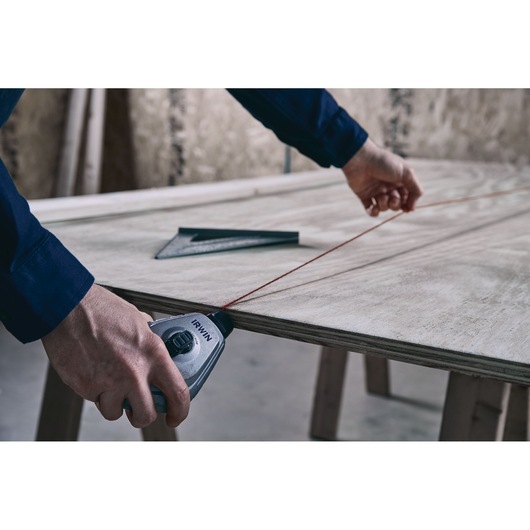 Photo of IRWIN chalk line tool 1932890 marking a straight line on a plywood sheet in a workshop setting.
