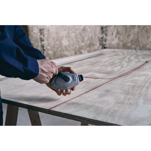 IRWIN chalk line tool 1932890 marking a straight red line on plywood sheet.