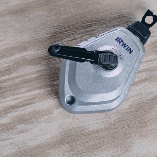 IRWIN 1932890 silver chalk line reel with black handle, top view on wood surface.
