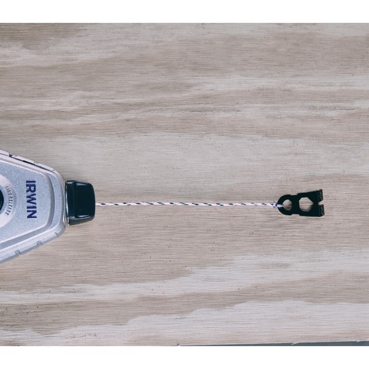 IRWIN chalk line reel 1932890, silver casing with blue logo, extended string and hook, top view on wood surface.