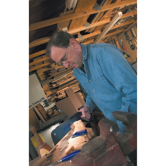 Photo of a person in a denim shirt using an IRWIN hand saw, 2011200, in a woodworking shop.