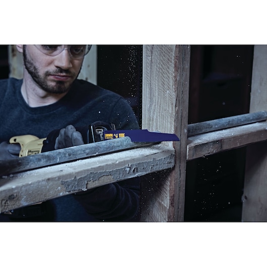 IRWIN 2018874 reciprocating saw blade cutting through wood window frame, close-up in action with gloved hand.