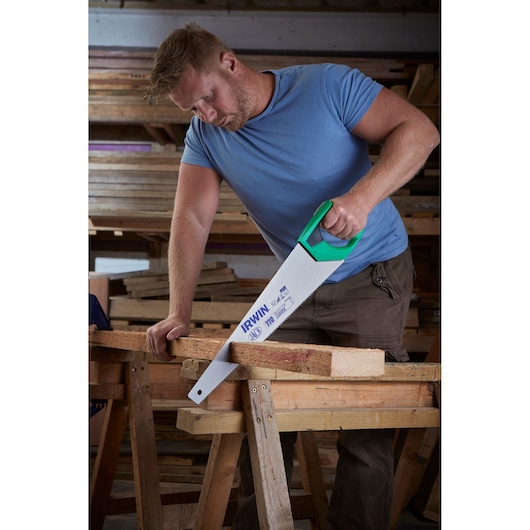 Photo of IRWIN 2028296 hand saw with green handle cutting wood on a workbench in a workshop.