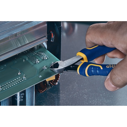 A close-up view of a hand using blue and yellow IRWIN diagonal cutting pliers to trim components on an electronic circuit board.