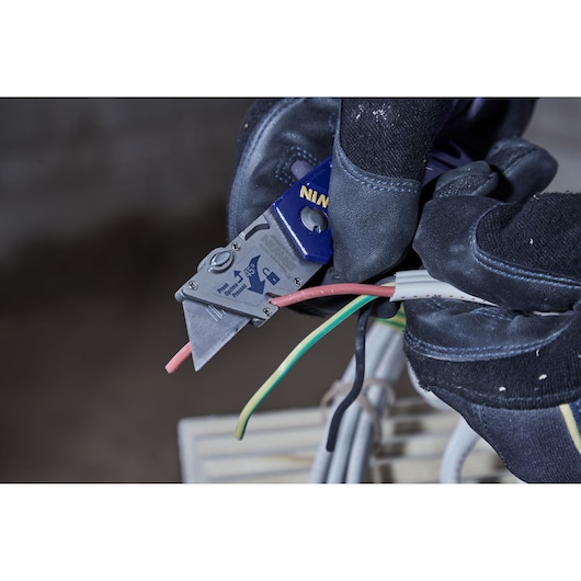 Photo of IRWIN utility knife SKU 2089100 cutting electrical wires, close-up with gloved hand.