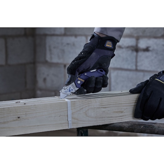 Photo of IRWIN utility knife SKU 2089100 cutting strap on wooden beam, worker wears gloves.