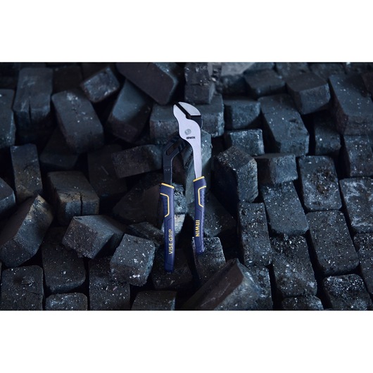 An IRWIN VISE-GRIP adjustable pliers with black and blue handles is positioned upright on a pile of dark, rough bricks.