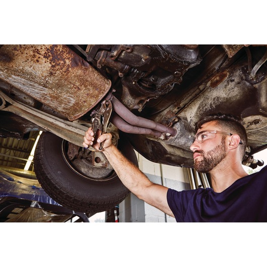 IRWIN IRHT82573 locking pliers being used to grip exhaust pipe under car in garage, close-up of tool in action.