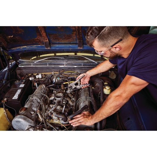 Photo of a person using an IRWIN adjustable wrench IRHT82573 to work on a car engine in a garage.