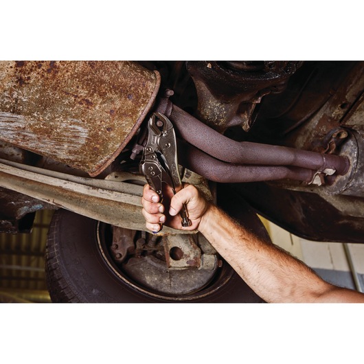 IRWIN IRHT82573 locking pliers gripping a bolt on a rusty exhaust under a vehicle, shown in use.