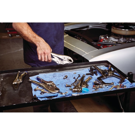 IRWIN IRHT82573 locking pliers held by a person near a mechanic's tray with assorted hand tools and parts.