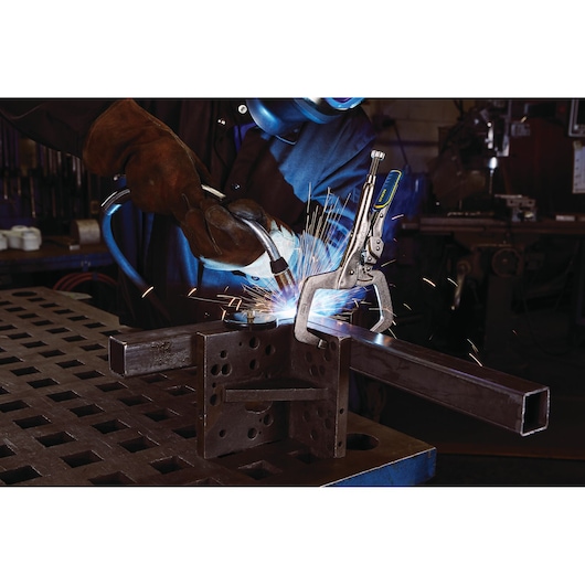 IRWIN IRHT82584 welding clamp holding metal pieces while sparks fly during welding in workshop.