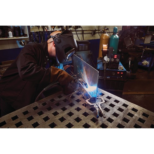 IRWIN IRHT82584 welding clamp secures metal sheet during welding in workshop, sparks flying, close-up.