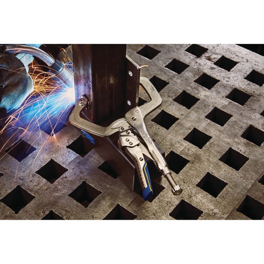 IRWIN IRHT82586 welding clamp securing metal on a workbench with visible sparks and welding torch.