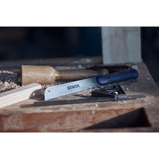 Photo of IRWIN 2011491 saw with blue handle on a woodworking bench, surrounded by wood shavings and tools.
