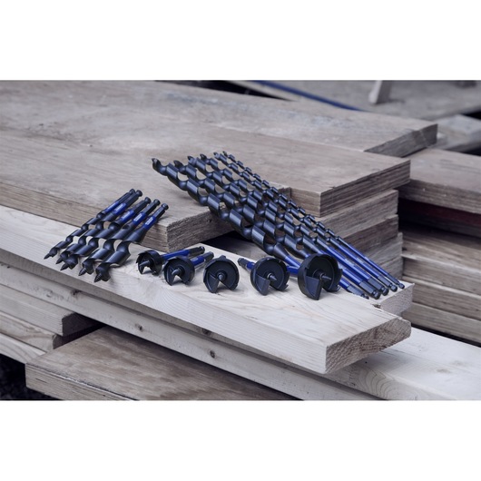 A set of blue and black auger drill bits displayed on stacked wooden planks in a workshop setting.