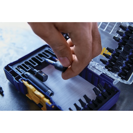 Close-up photo of a hand selecting a bit from an IRWIN IWAF1326 screwdriver bit set in a blue and yellow case.