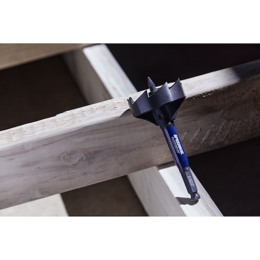 An IRWIN Speedbor drill bit with a blue shaft and large black cutting head, resting on unfinished wooden beams.