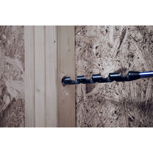 IRWIN IWAX3009 auger drill bit boring through wooden stud, side angle, with wood chips around the hole.