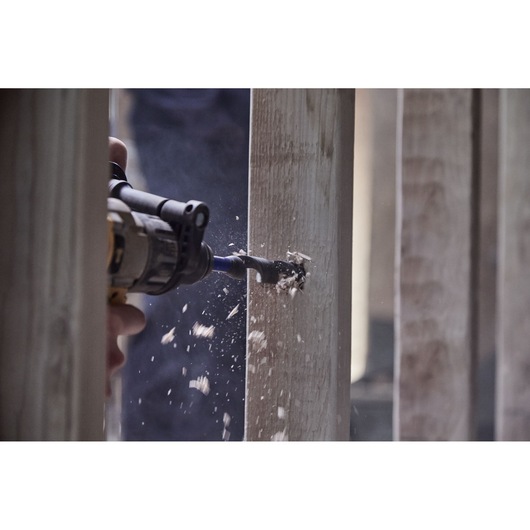 IRWIN drill bit IWAX3017 in a power drill cutting through wood, close-up with wood shavings flying.