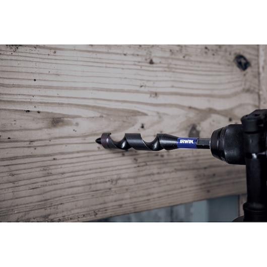 IRWIN IWAX3018 auger drill bit in use drilling through light wood, side view, photography.
