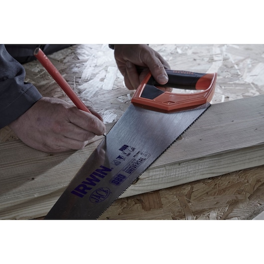 IRWIN hand saw IWHT20385-3 used to mark a cut line on a wooden board with a pencil, close-up view.