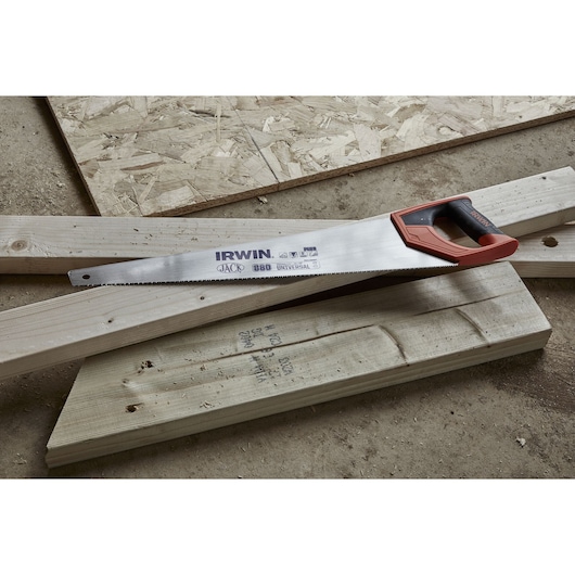 An IRWIN hand saw with a black and red handle resting on pieces of lumber and wooden boards.