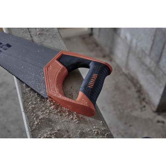 Photo of IRWIN hand saw IWHT20385-3 with black and orange handle resting on wood, sawdust visible.